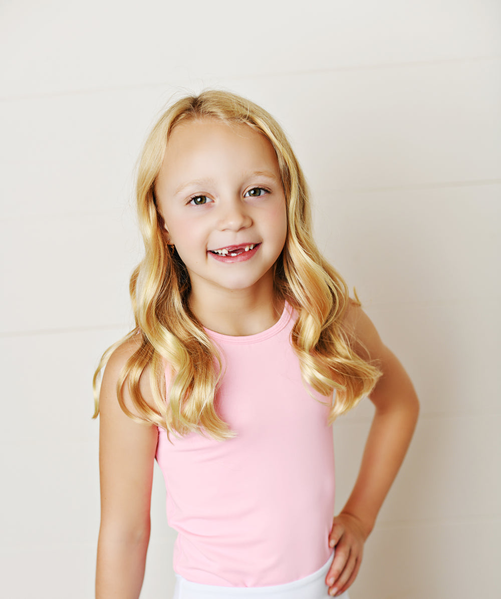 Young girl wearing a pink tank top against a plain background