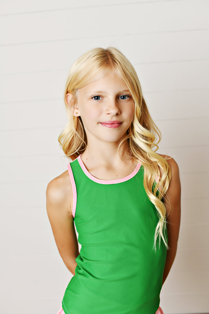 Young girl wearing a green tank top with pink trim against a plain background