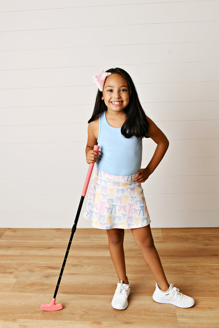 Young girl holding a pink and black toy golf club on a wooden floor with a white wall background