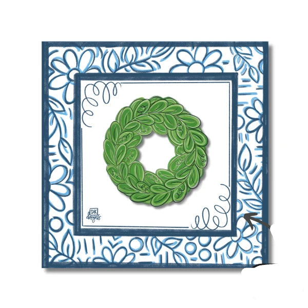 A square decorative card or art print featuring a green leaf wreath centered on a white background, surrounded by layered blue borders and a blue floral patterned frame. 