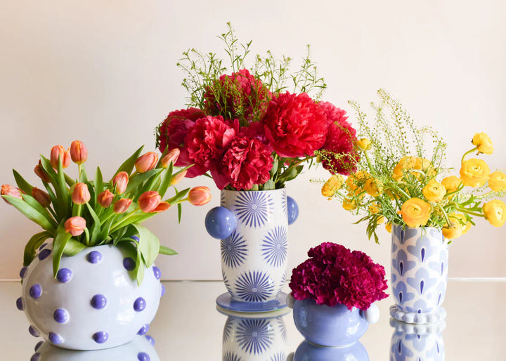 Decorative vases with polka dot patterns containing flowers on a white background