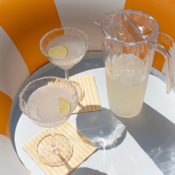 Two martini glasses with lemon slices and a pitcher of lemonade on a striped surface.