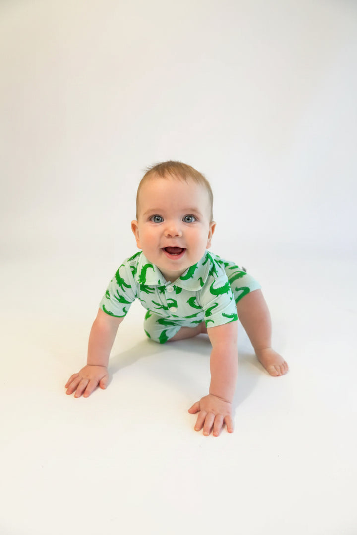 Baby wearing a green and blue alligator patterned onesie on a white background
