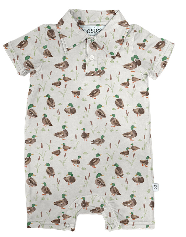 A baby short-sleeve polo romper with an all-over duck print on a light cream background. The print features brown ducks with green heads and small green reeds.