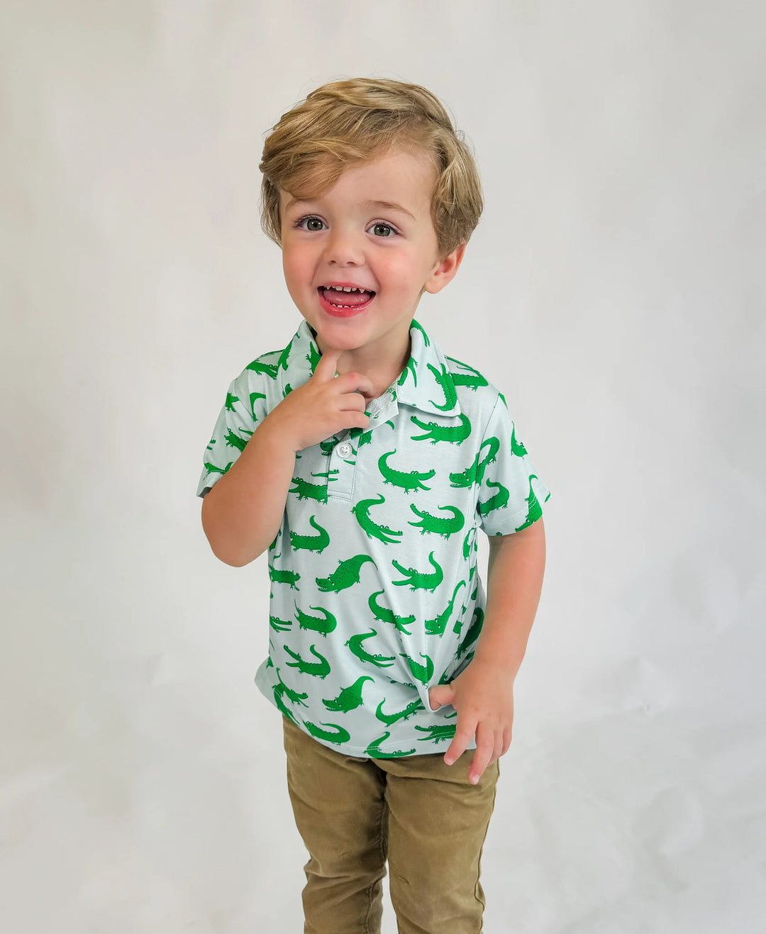 Child wearing a green shirt with dinosaur pattern on a plain background