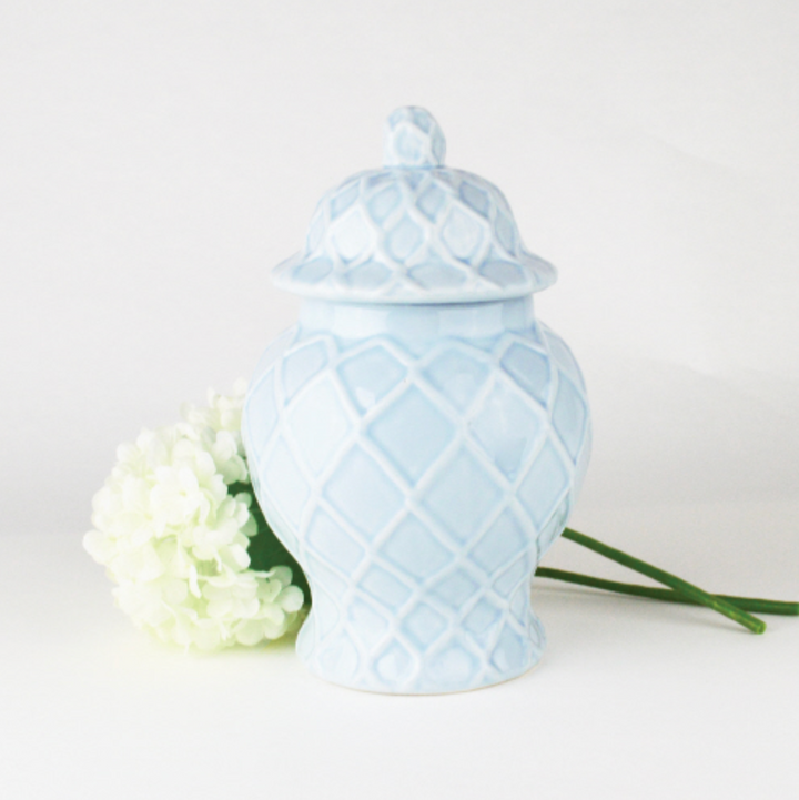 A light blue textured small ginger jar with a floral pattern, displaying a bouquet of white flowers and green leaves peeking out from the top.