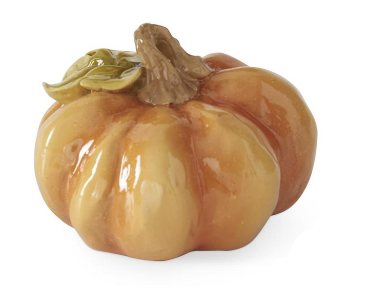 A glossy ceramic decorative pumpkin figurine in warm orange and yellow tones with a brown stem and small green leaves, shown on a white background.