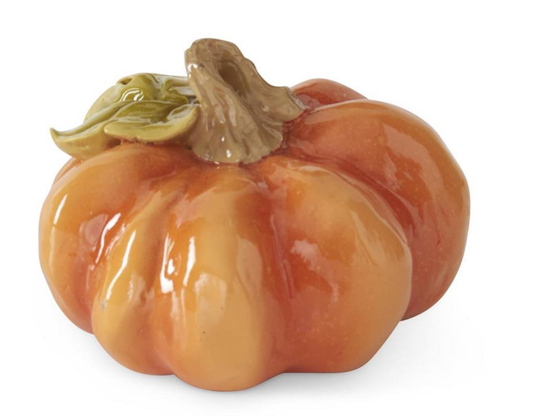 A glossy ceramic decorative pumpkin in shades of orange and yellow with a brown stem and green leaf detail, shown on a white background 