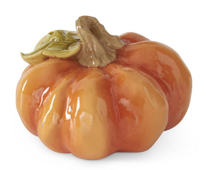 A glossy ceramic decorative pumpkin in shades of orange and yellow with a brown stem and green leaf detail, shown on a white background 