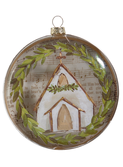 A round clear glass Christmas ornament featuring a painted white church with a green wreath, surrounded by a green laurel wreath and scriptural text background.