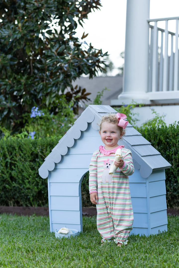 LITTLE GIRL WEARING MULTI STRIPE PUPPY APPLIQUE RUFFLE ROMPER NEXT TO BLUE DOG HOUSE