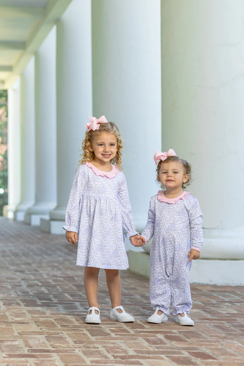 LITTLE GIRL WEARING HIDDEN CASTLE FLORAL DRESS ON BRICK STEPS WITH YOUNGER GIRL IN MATCHING ONSIE OUTFIT