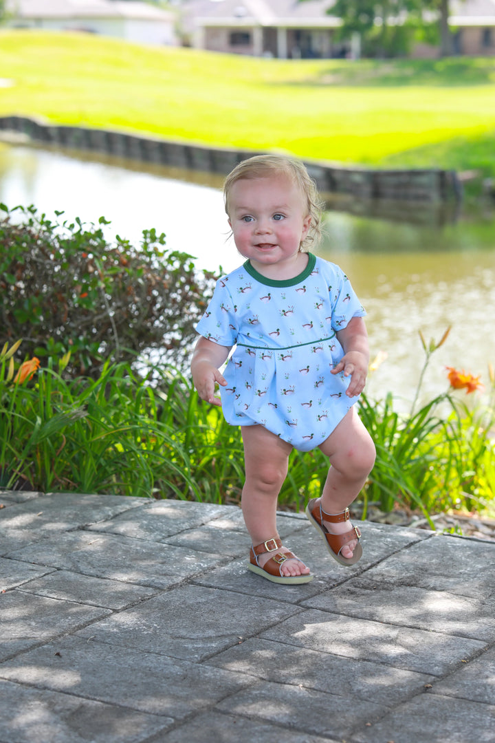 LITTLE BABY BOY STANDING NEXT TO A POND WEARING BLUE OUTFIT WITH GREEN TRIM AND DUCK DESIGN