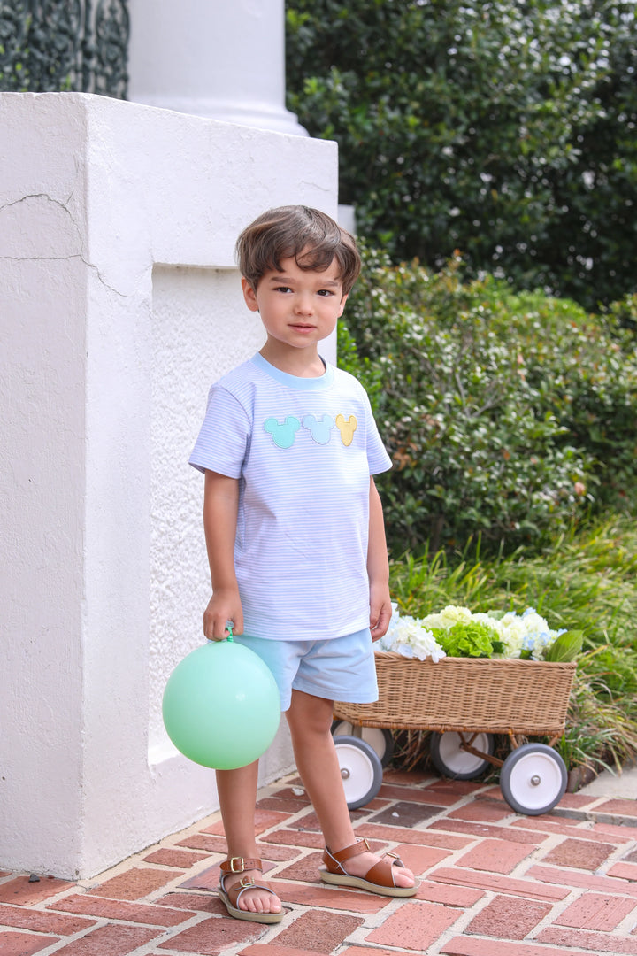 LITTLE BOY STANDING NEXT TO WHITE WALL WITH BALLOON WEARING BLUE AND WHITE STRIPE SHORT SET WITH DISNEY EARS
