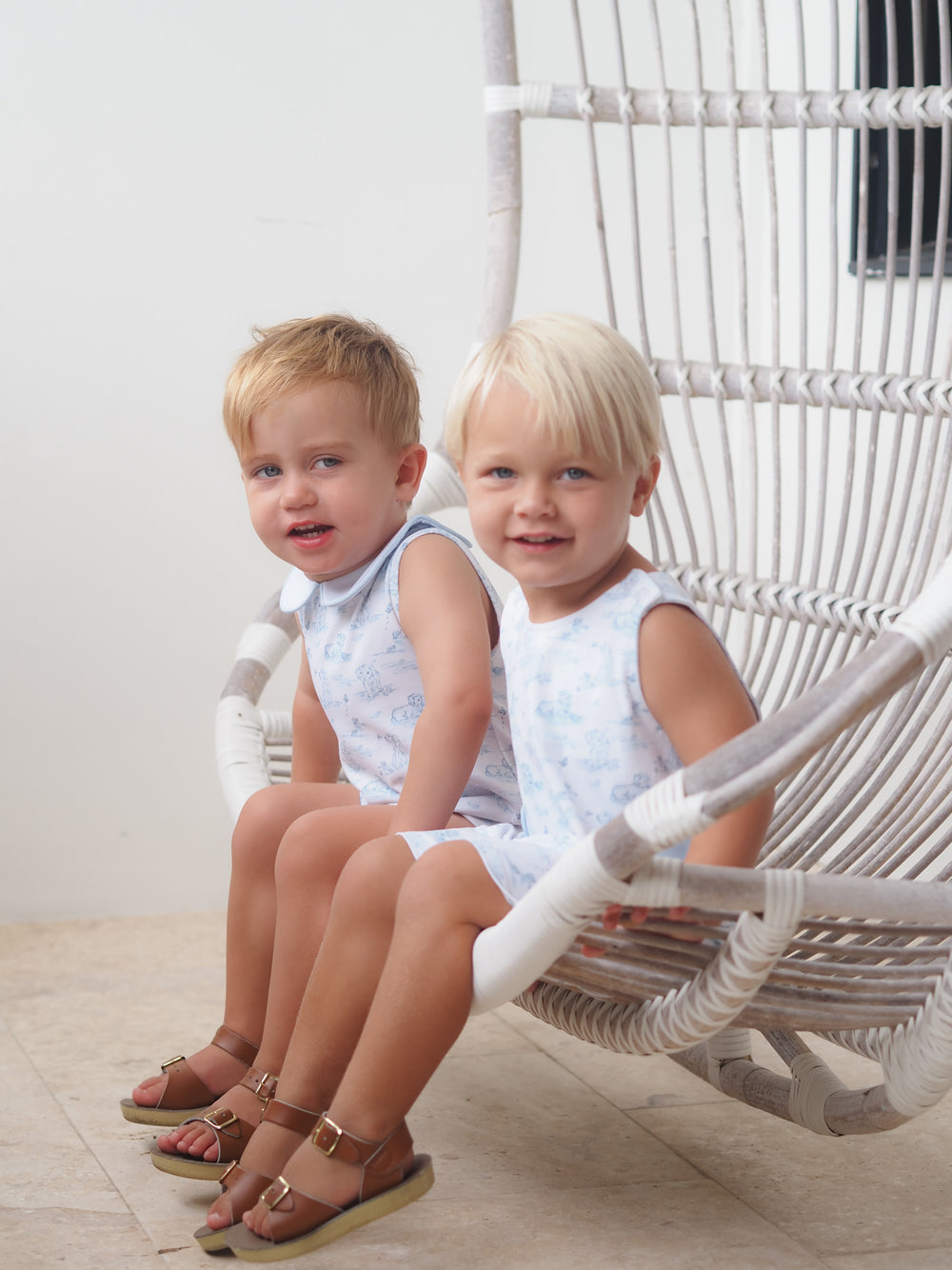 Two children sitting on a white wicker chair indoors.