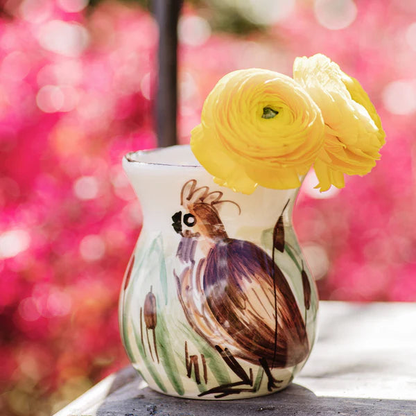 Decorative vase with a bird design and yellow flowers against a blurred pink background
