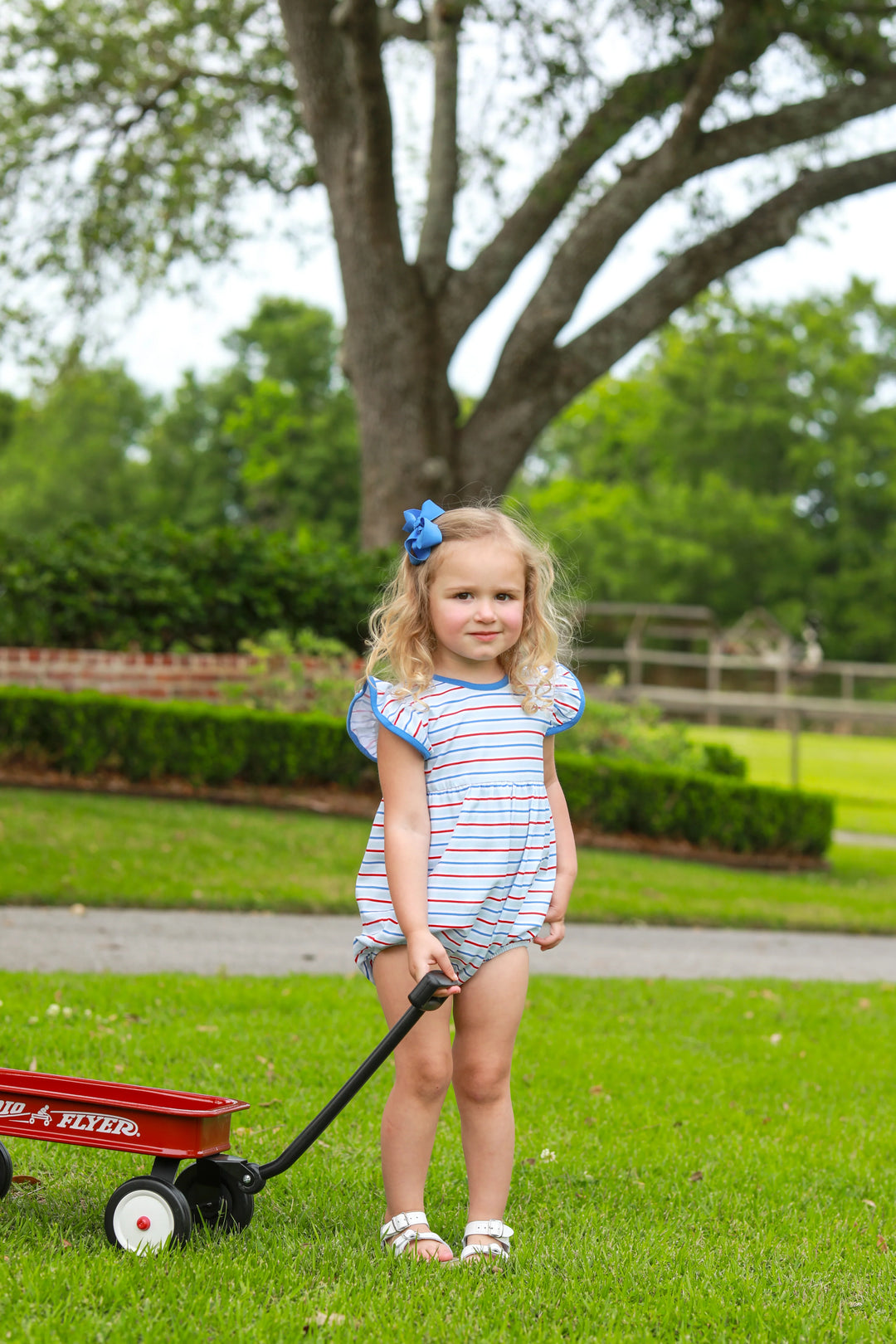 LITTLE GIRL IN THE GRASS PULLING A RED WAGON IN A BLUE RED AND WHITE FLUTTER SLEEVE PATRIOTIC BUBBLE