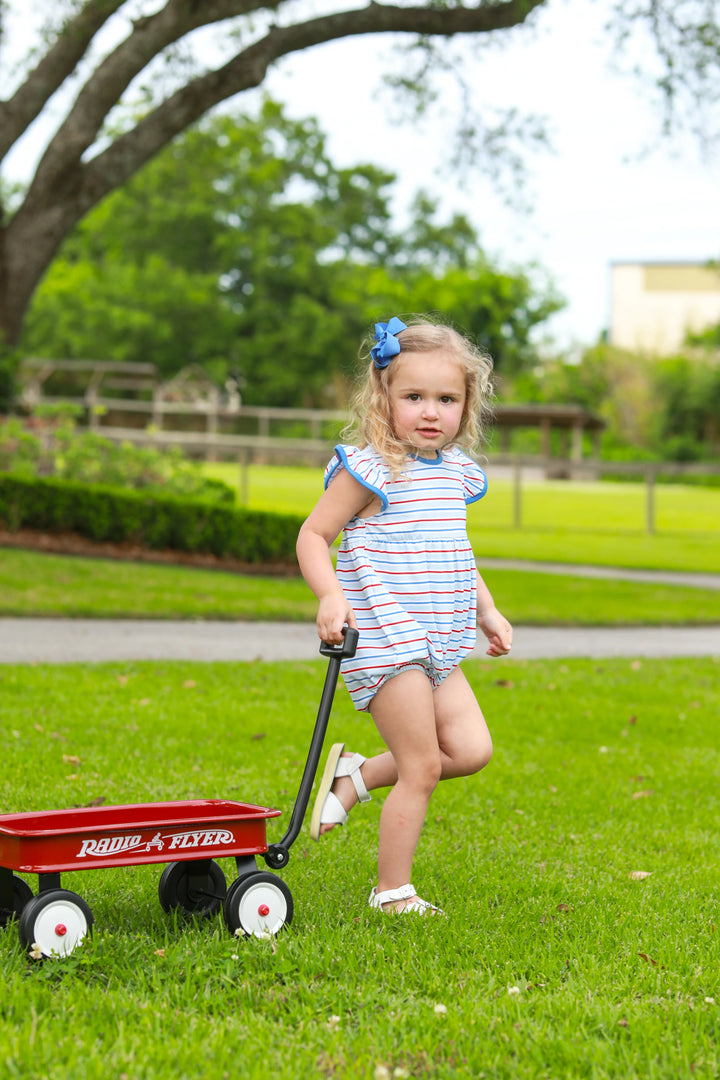 LITTLE GIRL IN THE GRASS PULLING A RED WAGON IN A BLUE RED AND WHITE FLUTTER SLEEVE PATRIOTIC BUBBLE