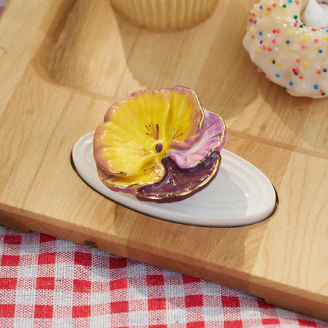 Colorful ceramic flower on a white plate with a wooden tray and checkered tablecloth in the background