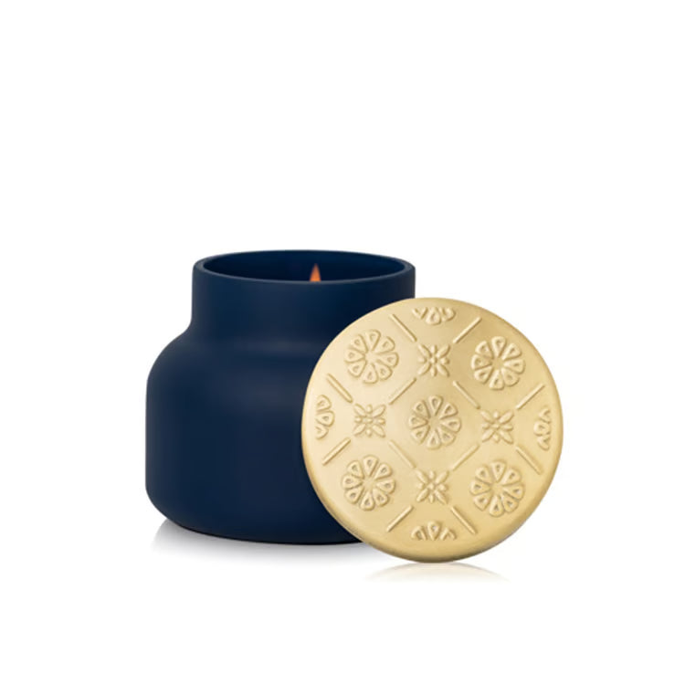 Navy blue candle with a gold lid featuring snowflake patterns on a white background