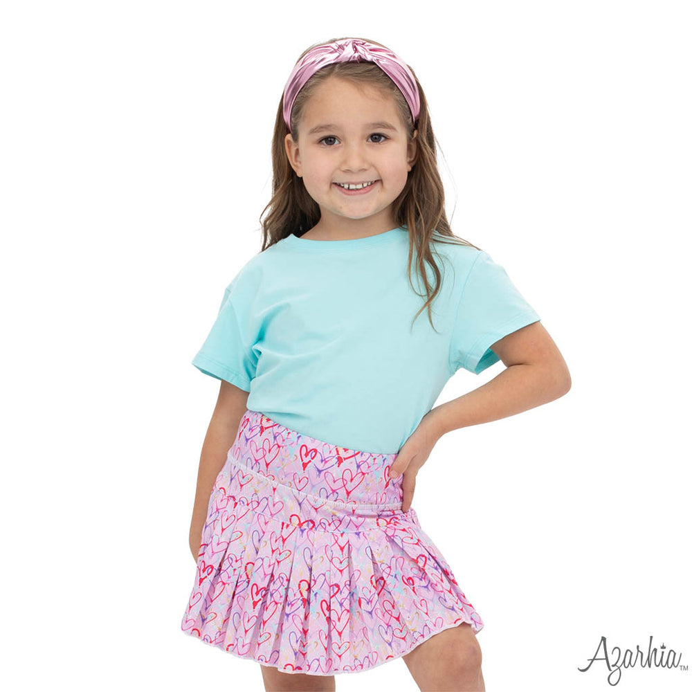 Young girl wearing a light blue shirt and pink heart-patterned skirt on a white background