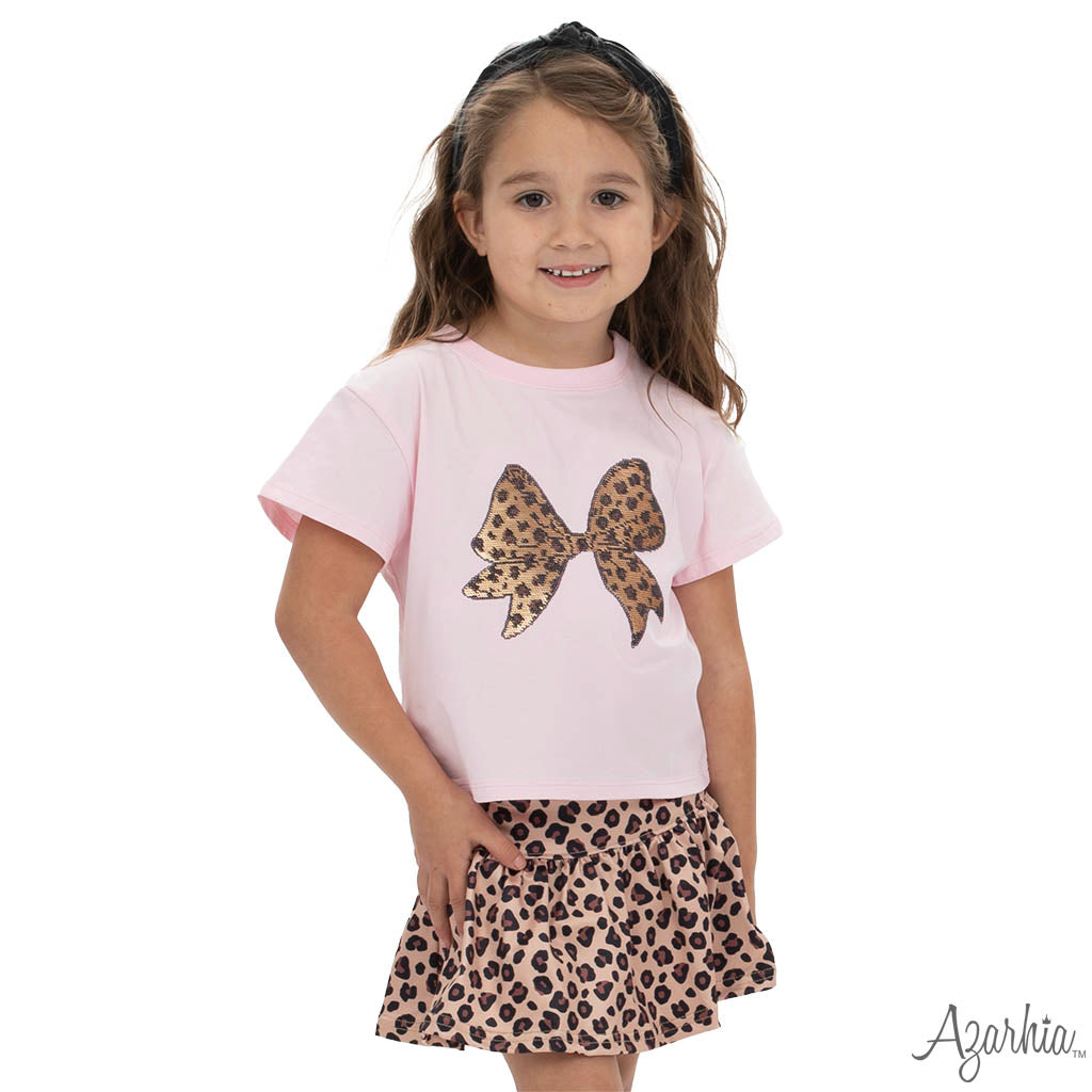 Young girl wearing a pink t-shirt with a leopard print bow and a matching skirt on a white background.