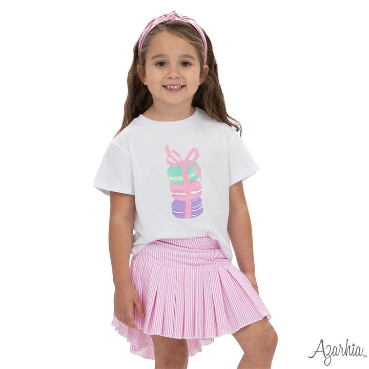 Young girl wearing a white t-shirt with colorful graphics and a pink pleated skirt on a white background.