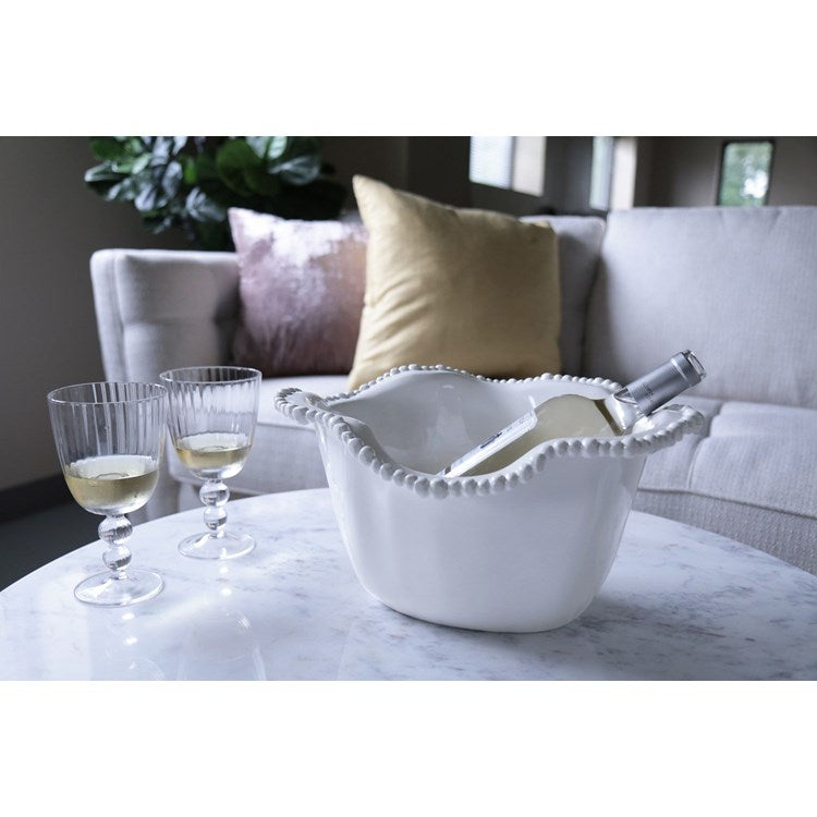 White melamine ice bucket with bottle and glasses on a marble surface with a couch in the background.