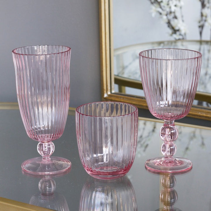 Three pink glass tumblers on a reflective surface with a mirror in the background.