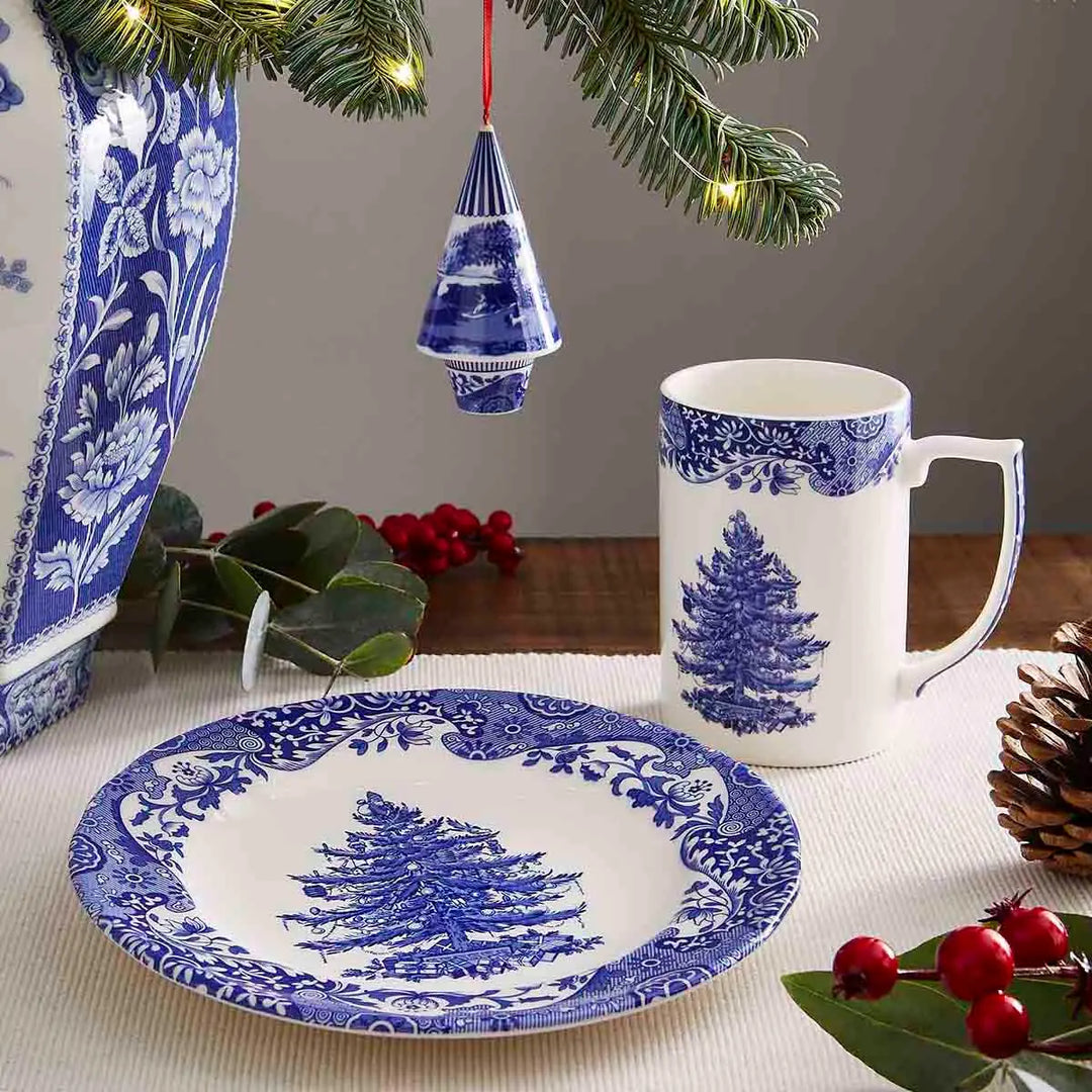 Blue and white Christmas-themed tableware set with a mug and plate on a tablecloth.