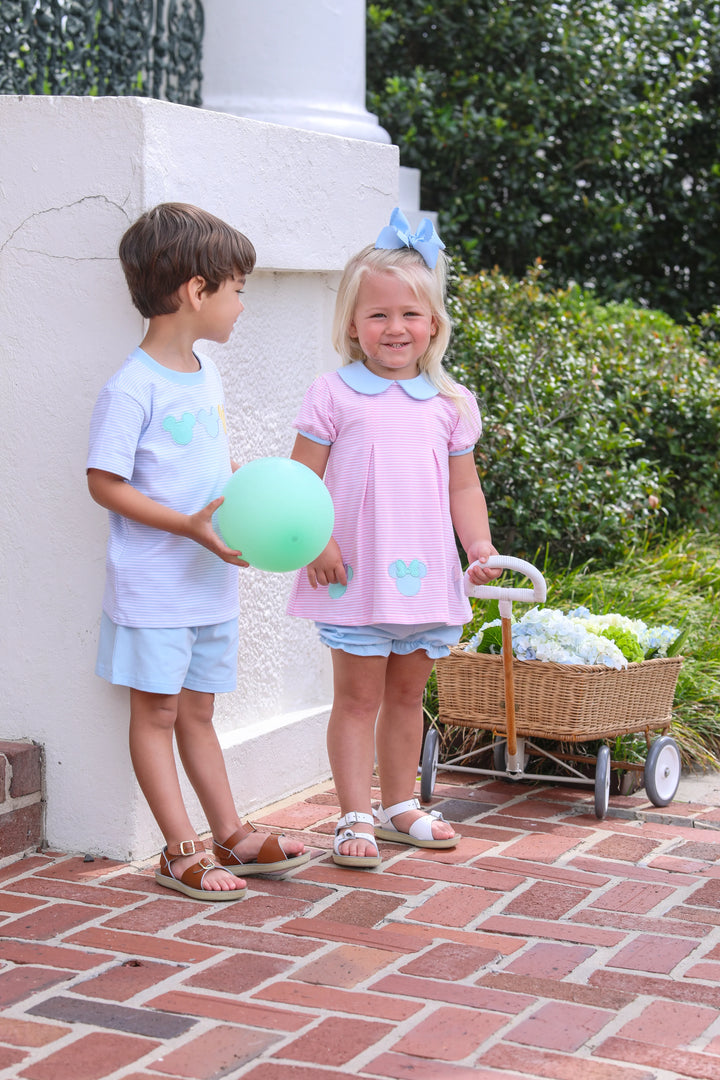 LITTLE BOY AND LITTLE GIRL WITH DISNEY OUTFITS ON STANDING NEXT TO WHITE WALL WITH BALLOONS AND WAGON FULL OF FLOWERS