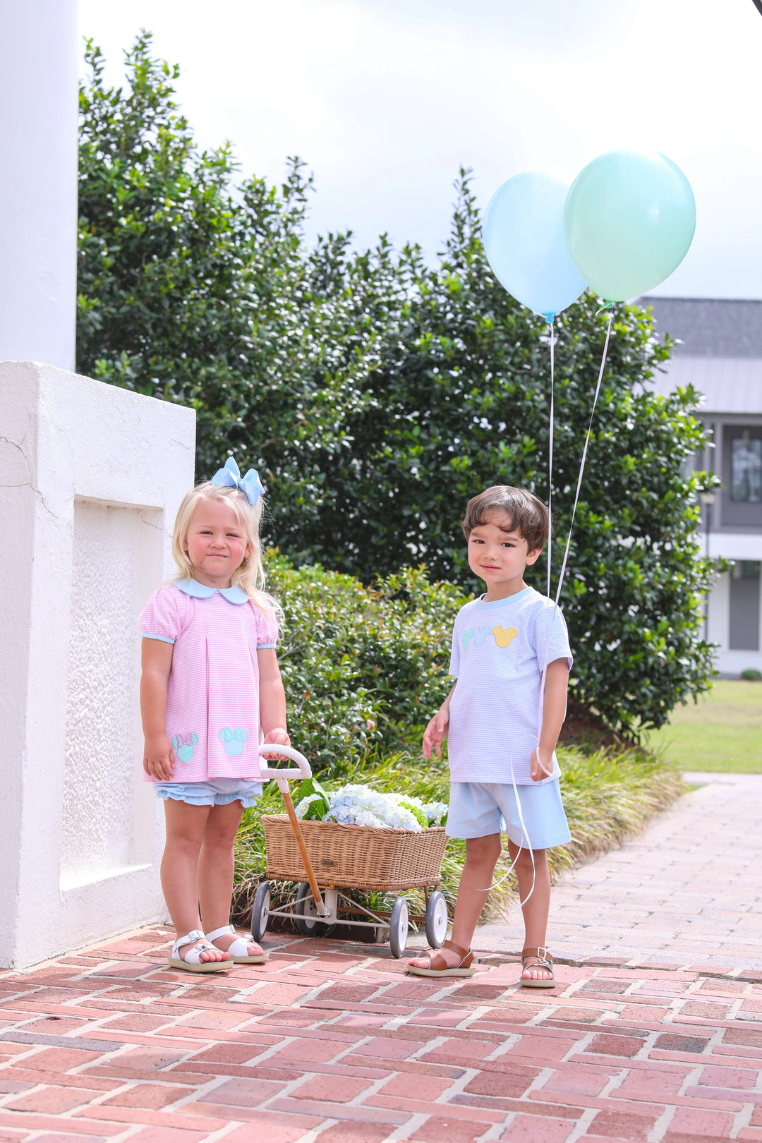 LITTLE BOY AND LITTLE GIRL WITH DISNEY OUTFITS ON STANDING NEXT TO WHITE WALL WITH BALLOONS AND WAGON FULL OF FLOWERS