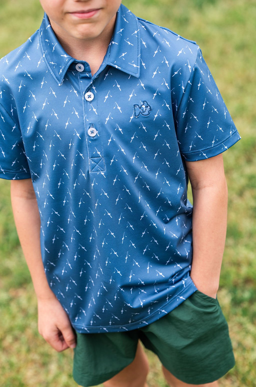 Child wearing a blue polo shirt with white patterns and green shorts outdoors.