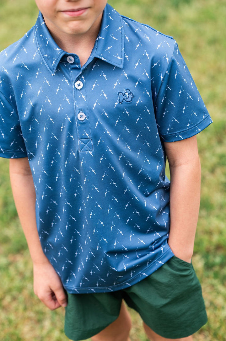 Child wearing a blue polo shirt with white patterns and green shorts outdoors.