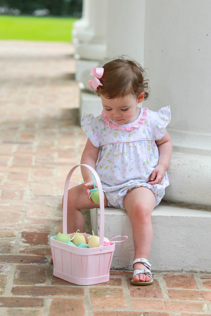 LITTLE GIRL SITTING ON COLUMN LOOKING AT HER EASTER EGGS IN EASTER BASKET WEARING WHITE AND PINK BUNNY MOTIF BUBBLE