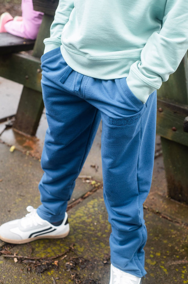 Person wearing blue pants and a light green jacket with a visible brand logo, standing on a concrete surface.