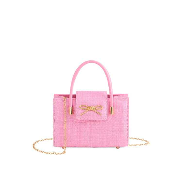 Pink woven bow clutch handbag with top handle and gold chain strap, featuring textured fabric and gold hardware | Walker Boutique