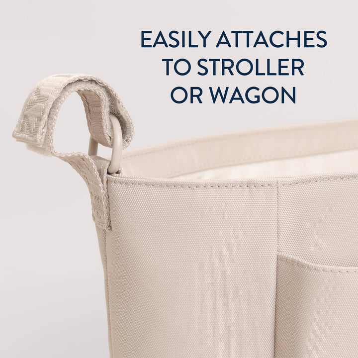 Close-up of a beige fabric storage basket with a loop handle, shown against a light gray background with dark blue text reading 'EASILY ATTACHES TO STROLLER OR WAGON'.