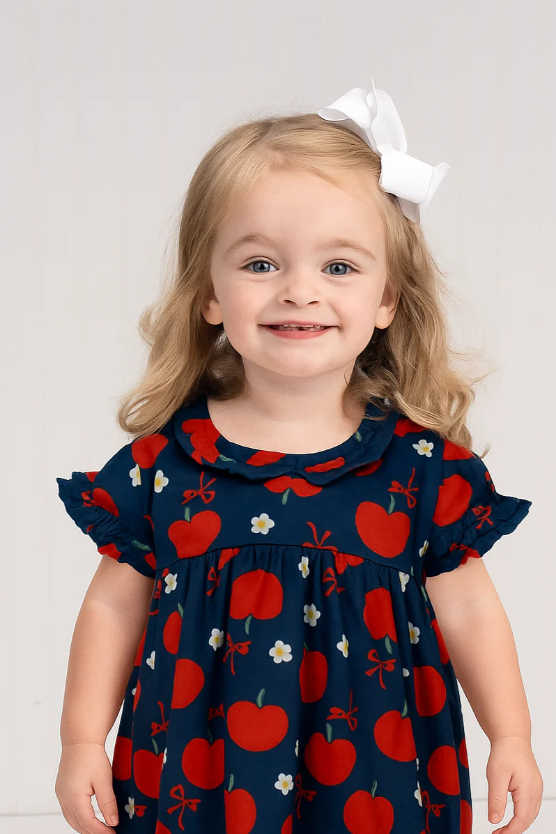 Child wearing a navy bubble with red apple pattern on a plain background
