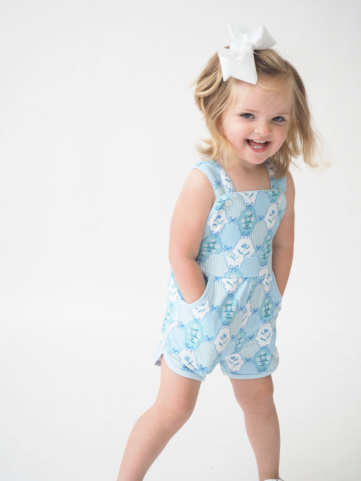 Child wearing a blue floral romper with a white bow on a white background