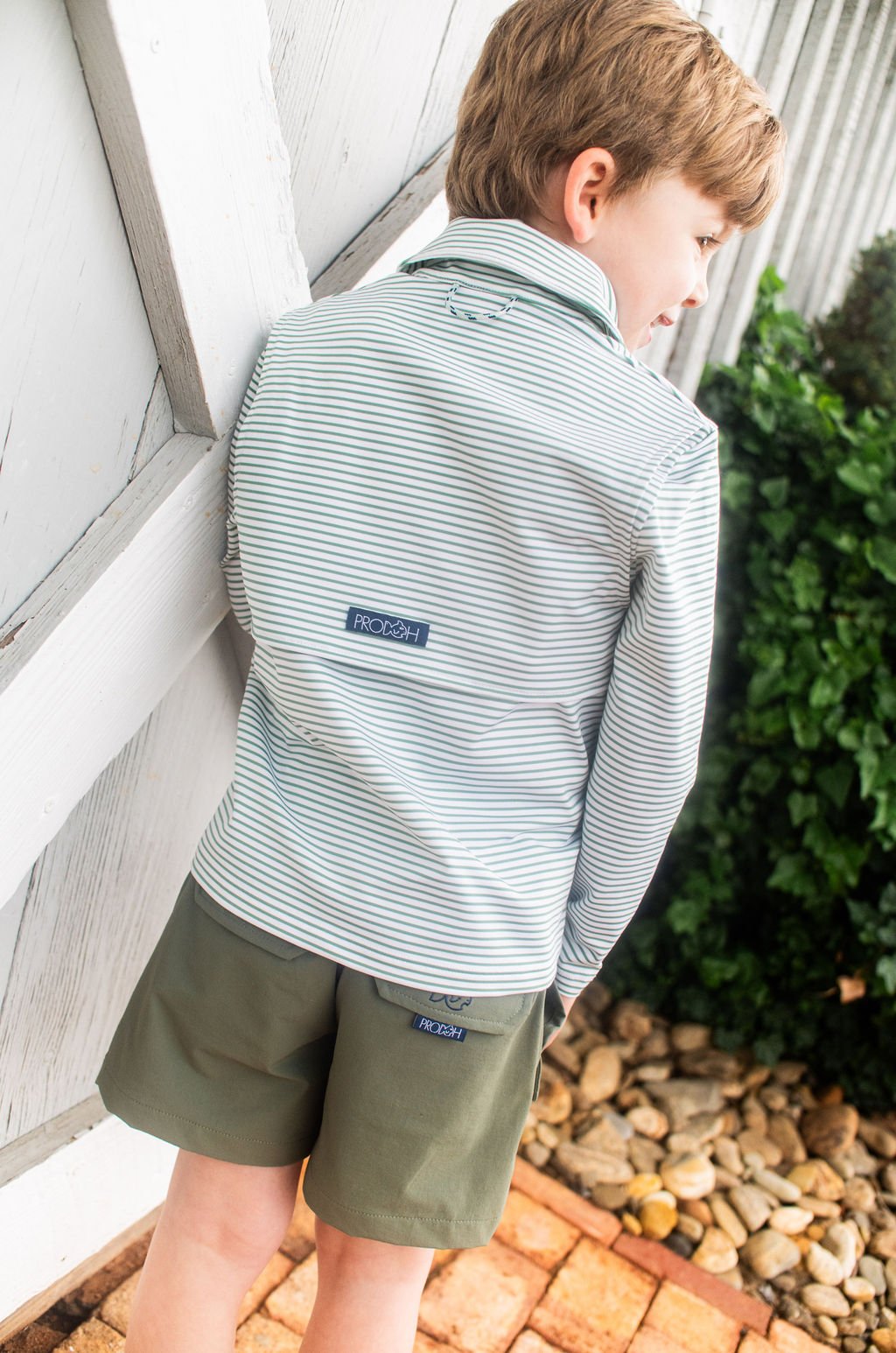 Child wearing a striped shirt and shorts with a visible brand logo, standing outdoors.