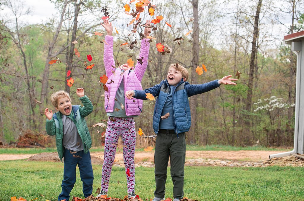 Three children playing with leaves in a backyard setting