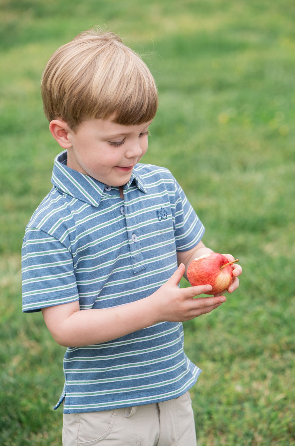 Young boy holding an apple outdoors on a grassy field
