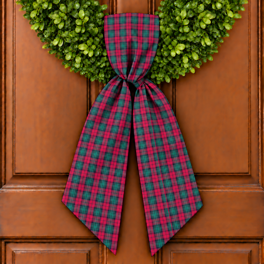 Red and green wreath sash on boxwood wreath on wooden door.