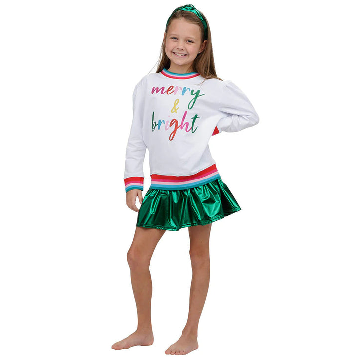 Young girl wearing a white sweater with colorful text and a green skirt on a white background