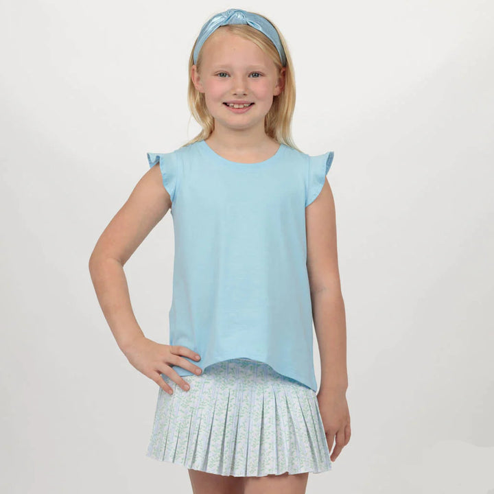 Young girl wearing a light blue top and pleated skirt with a headband, on a plain background.