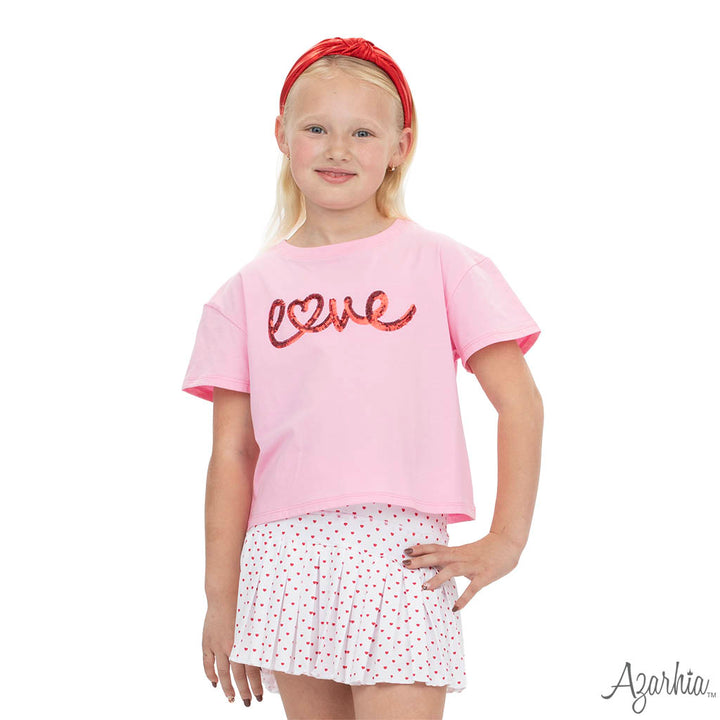 Young girl wearing a pink 'love' shirt and white skirt with red polka dots on a white background.