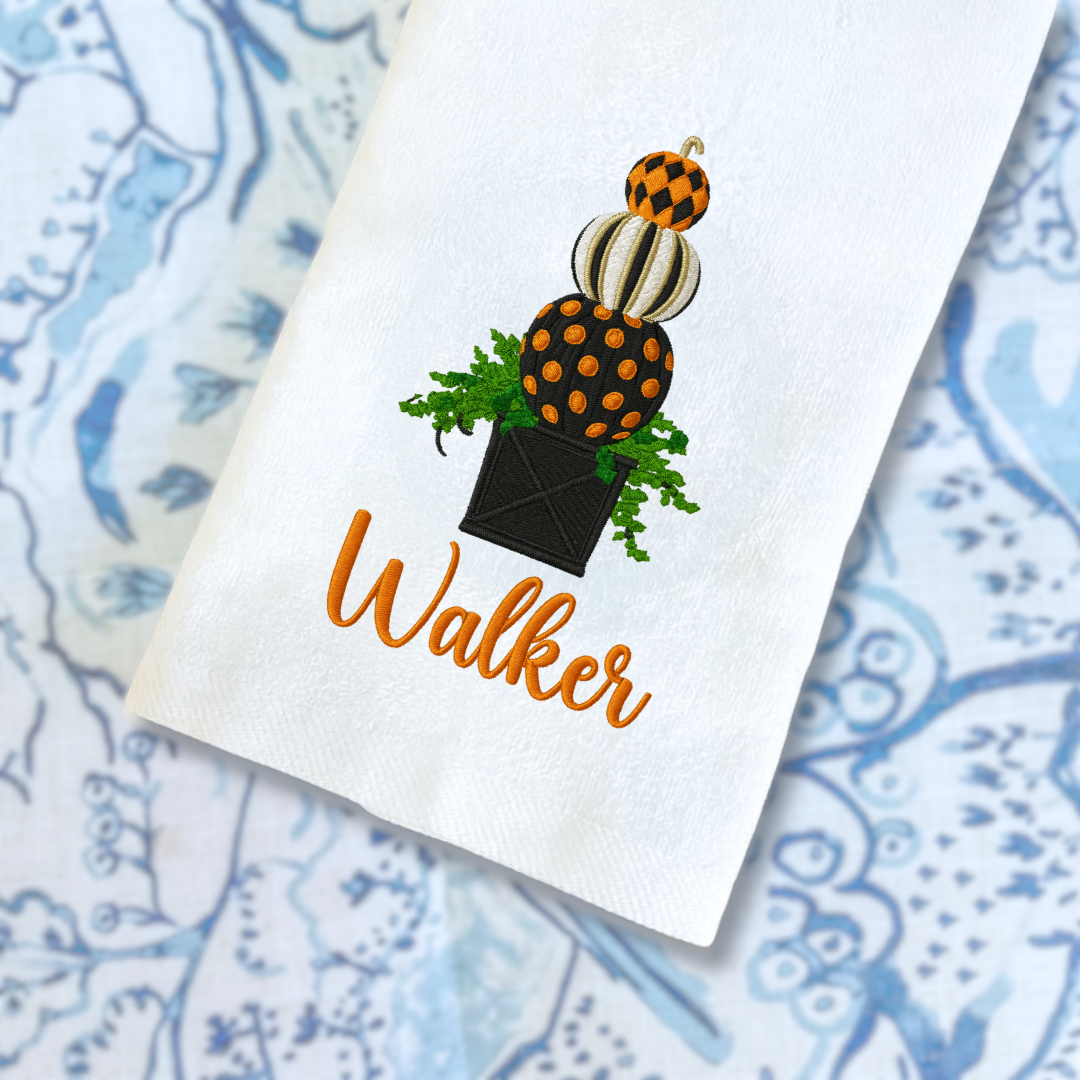 White towel with decorative pumpkins and the name 'Walker' on a blue patterned background