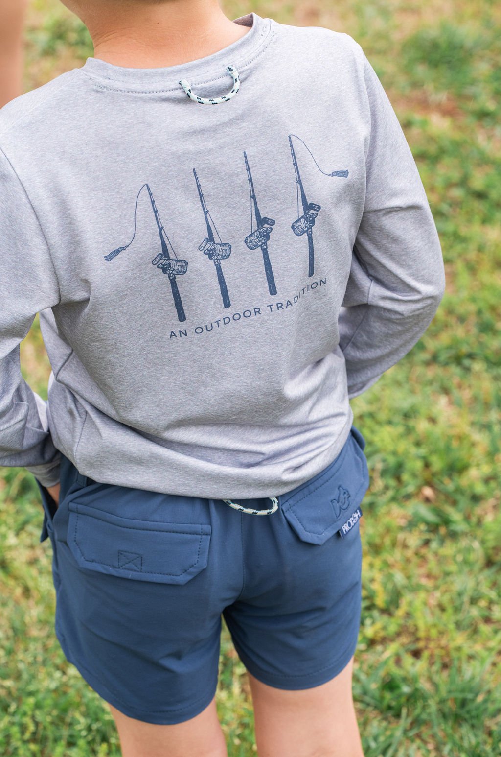 Person wearing a gray long-sleeve shirt with graphic design and blue shorts on a grassy background