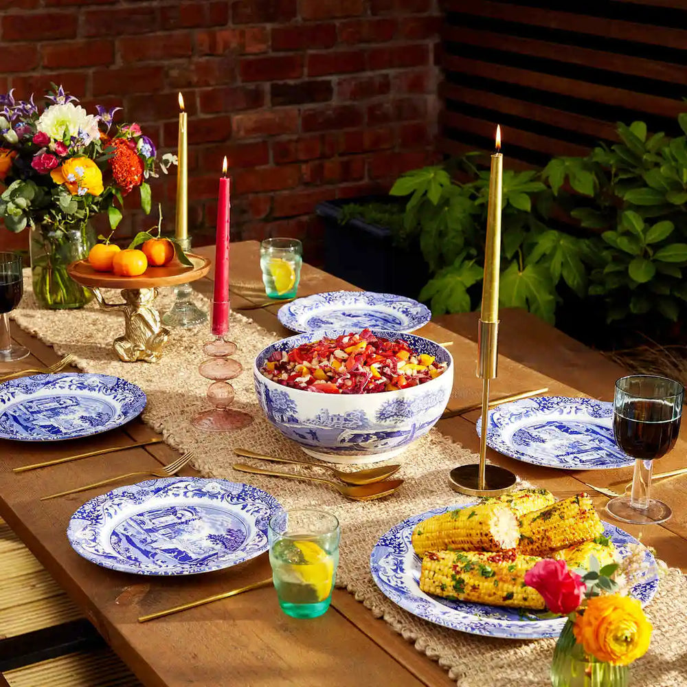 Dining table set with food, drinks, and decorative elements outdoors.